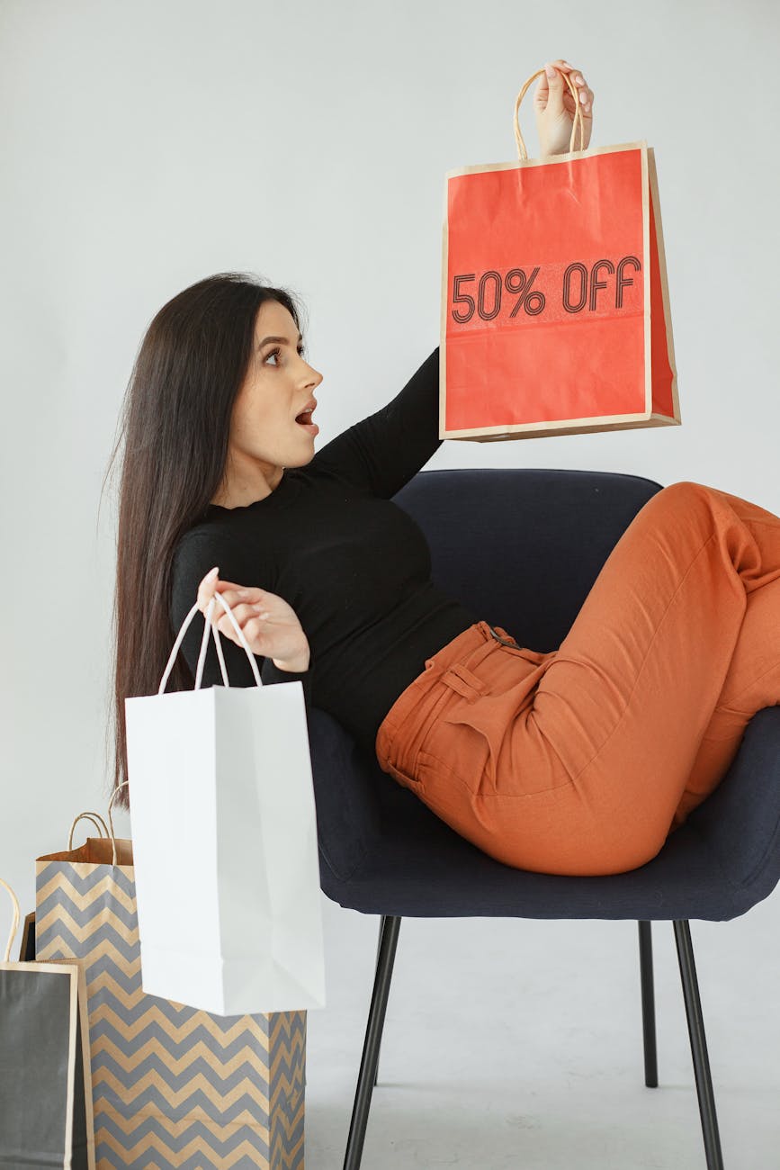 woman sitting on a chair and holding shopping bags from sale 5 Money Saving Tips to Protect Household Finances