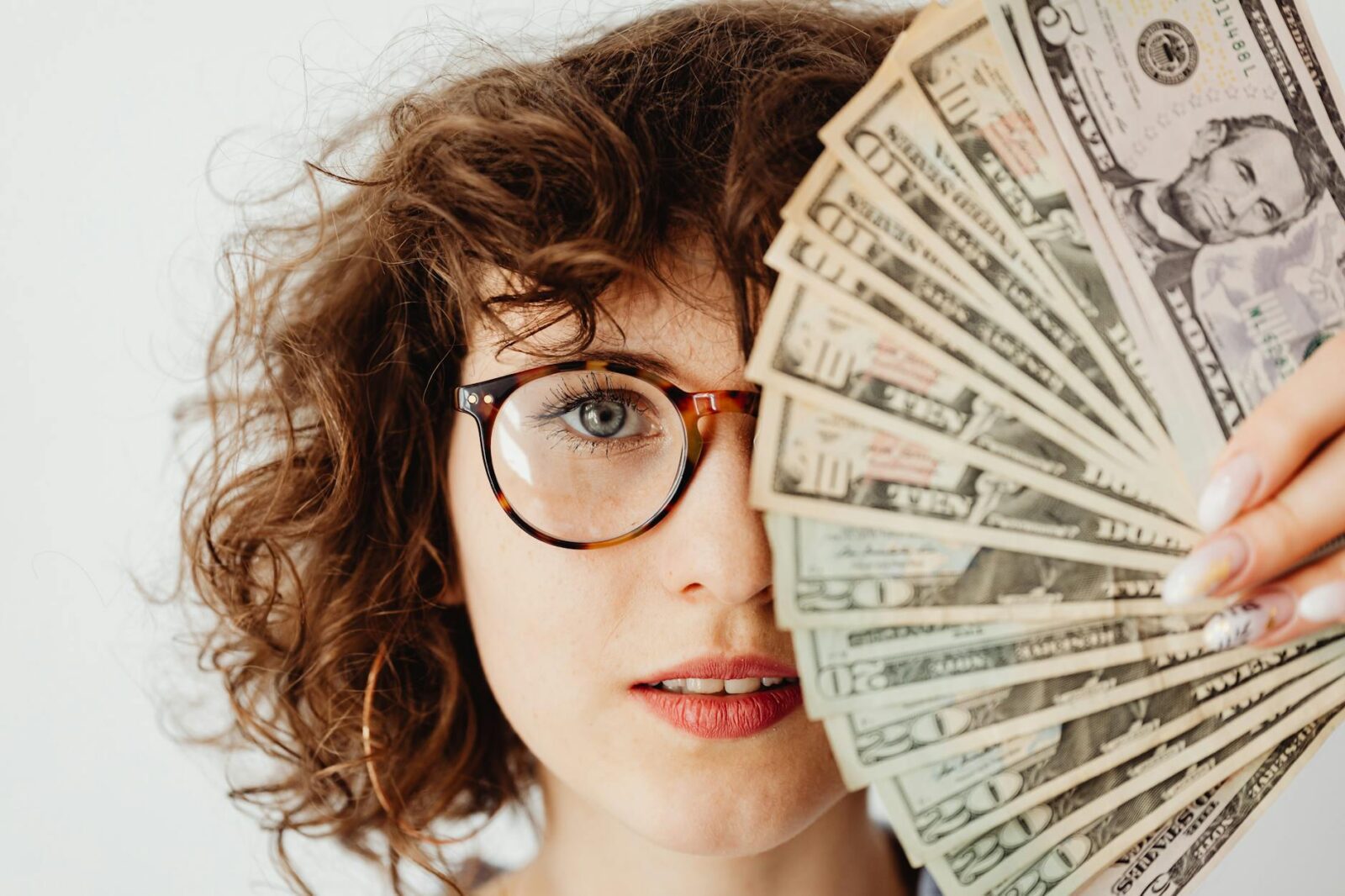 woman in eyeglasses covering her face with paper money The Biggest Life Milestones You Will Experience in Adulthood