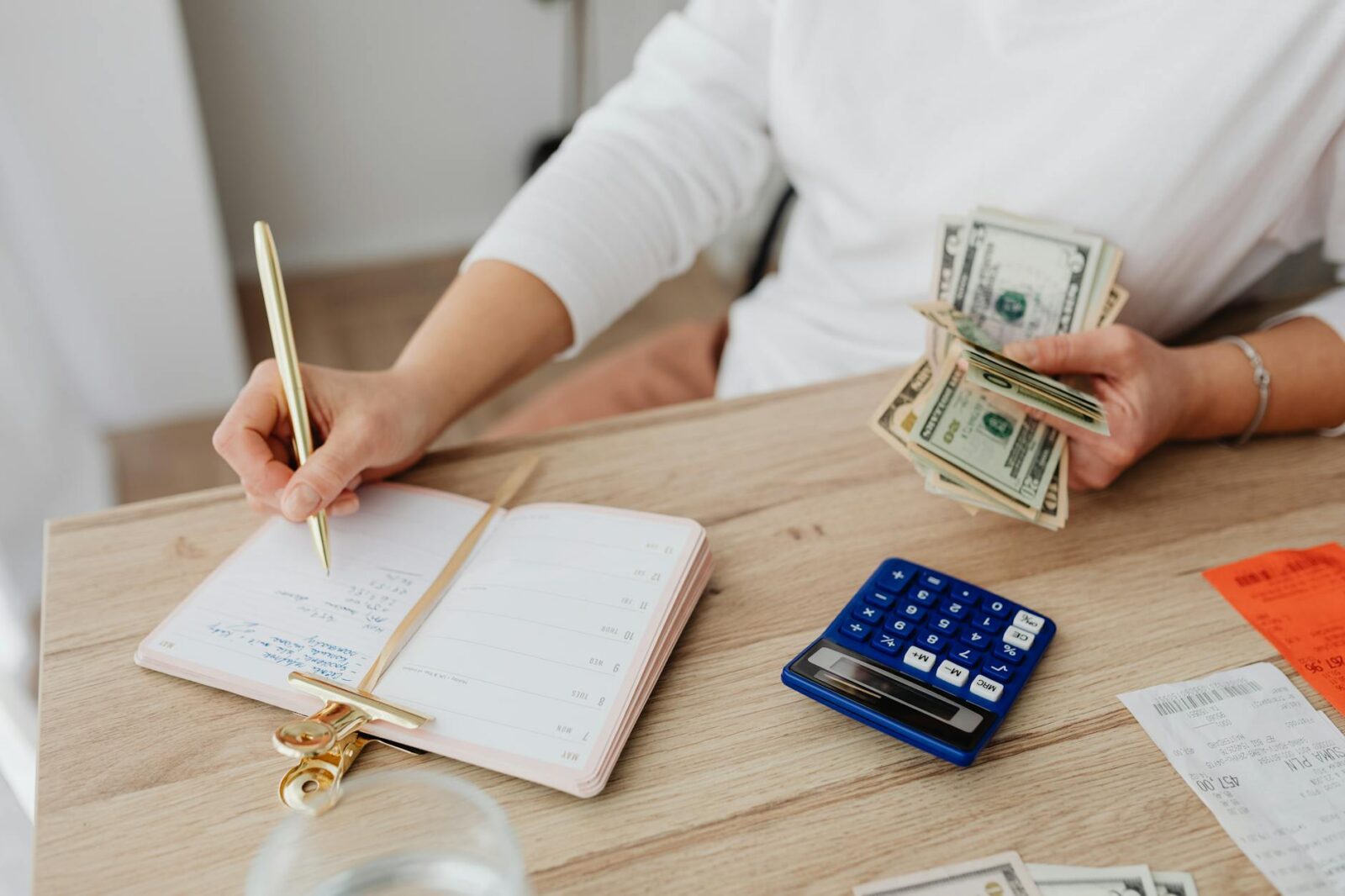 person writing on a notebook while holding money Budgeting for Shared Living: What to Expect and How to Split Costs