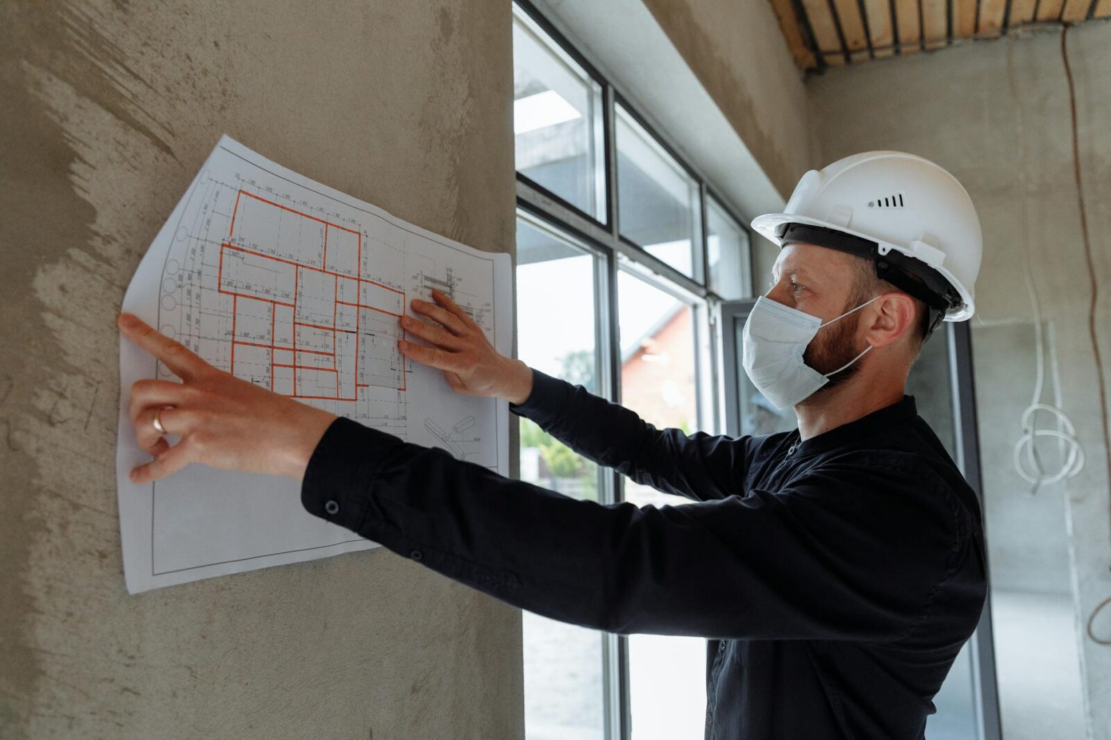 a man in black long sleeve shirt holding white paper on concrete wall The Biggest Renovation Mistakes People Are Still Making in 2025