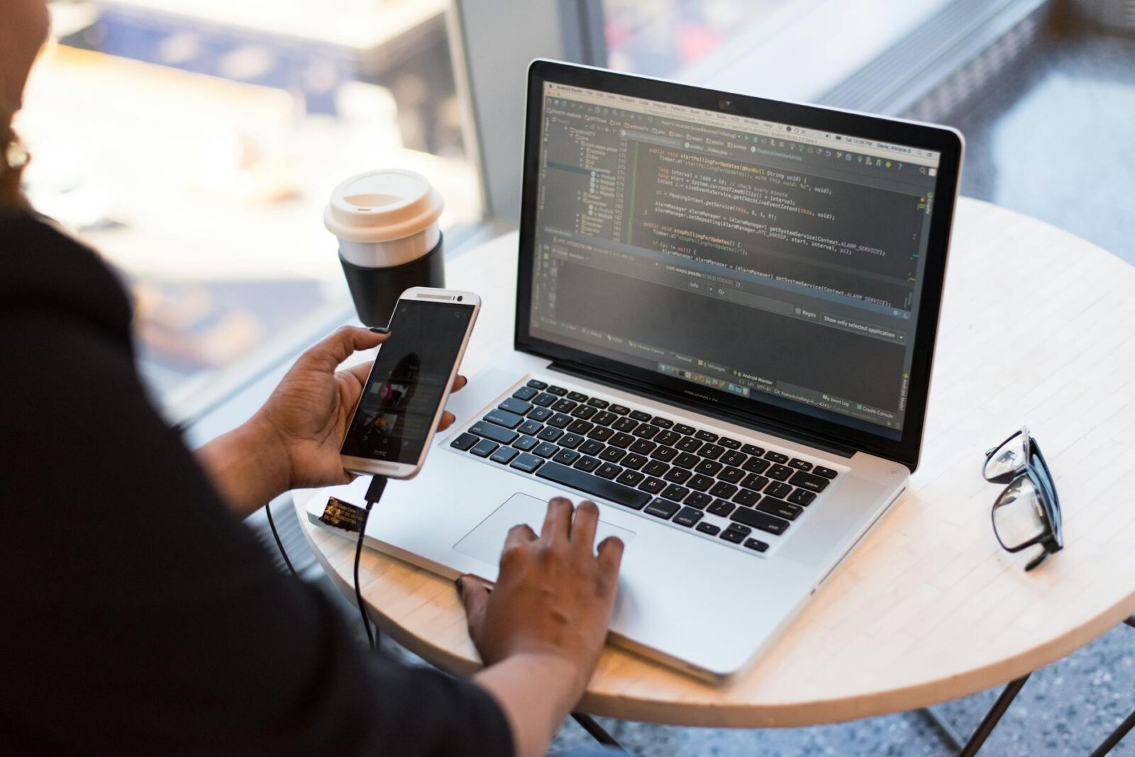 person holding smartphone while using laptop Tips for Choosing The Right Software Developer for Your Company