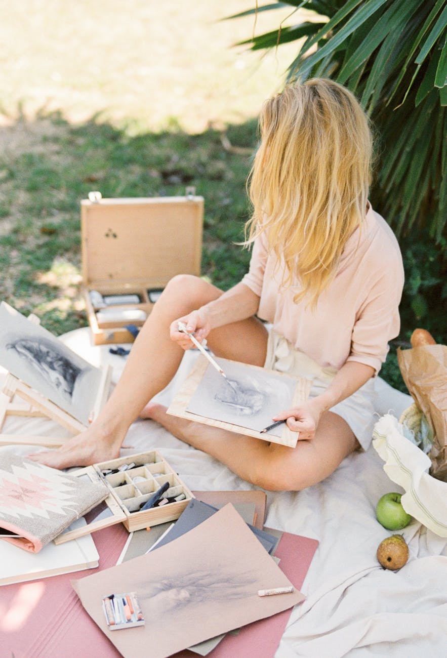 blonde woman sitting on white blanket sketching and painting on canvas 4 Unusual Hobbies That Break Free From The Mold