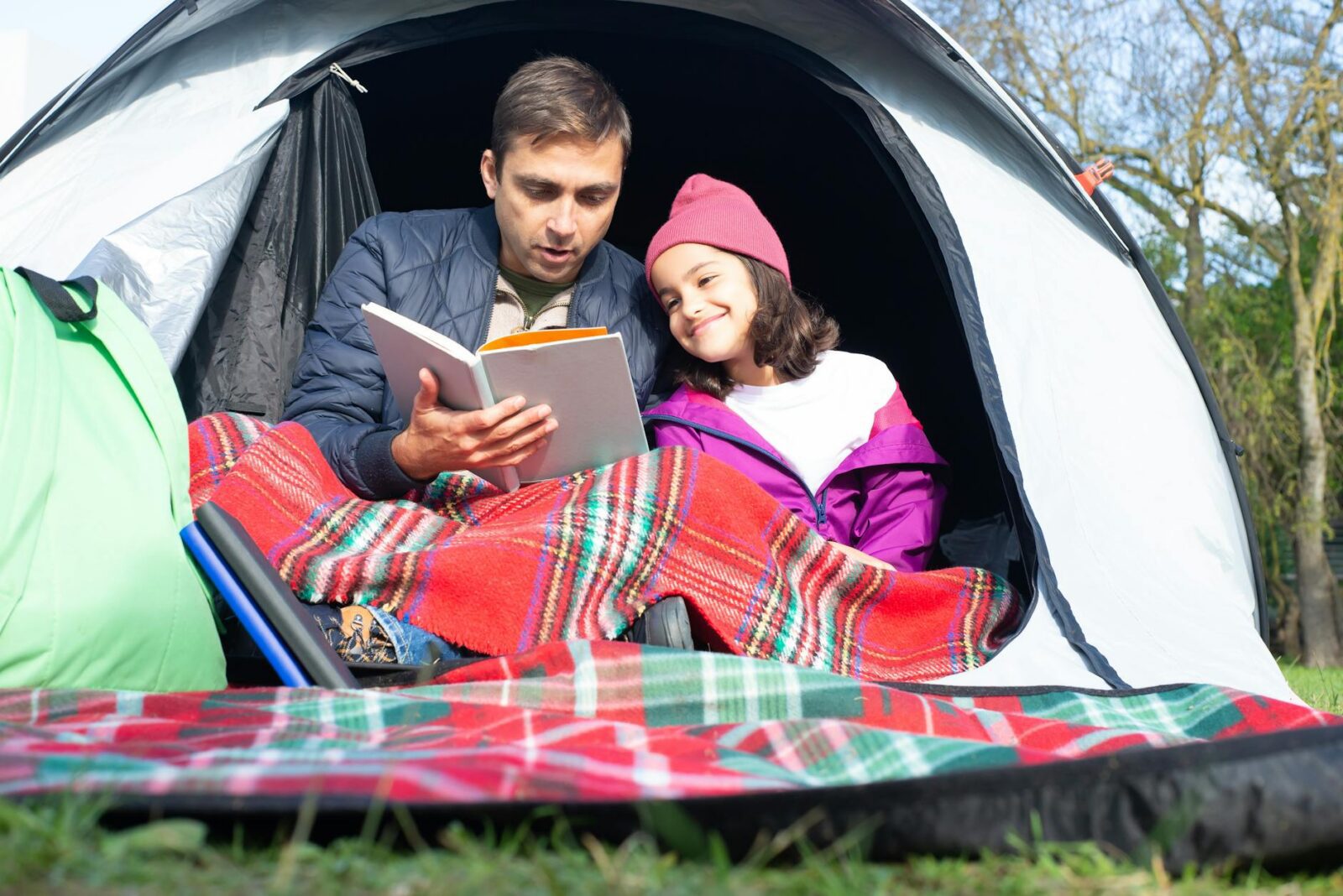 father and daughter reading a book while sitting inside the tent 7 Fun Family Vacation Ideas Your Kids Will Love