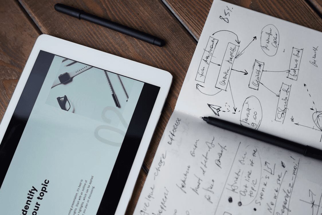 A tablet displaying a graphic alongside a notebook filled with handwritten notes and sketches on a wooden surface. 10 Proven Tips for Finding Help with Your Marketing Strategy