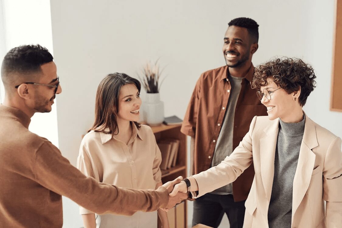 Four professionals engaging in a friendly handshake and conversation in an office setting. 10 Time-Saving Tricks to Improve Customer Service