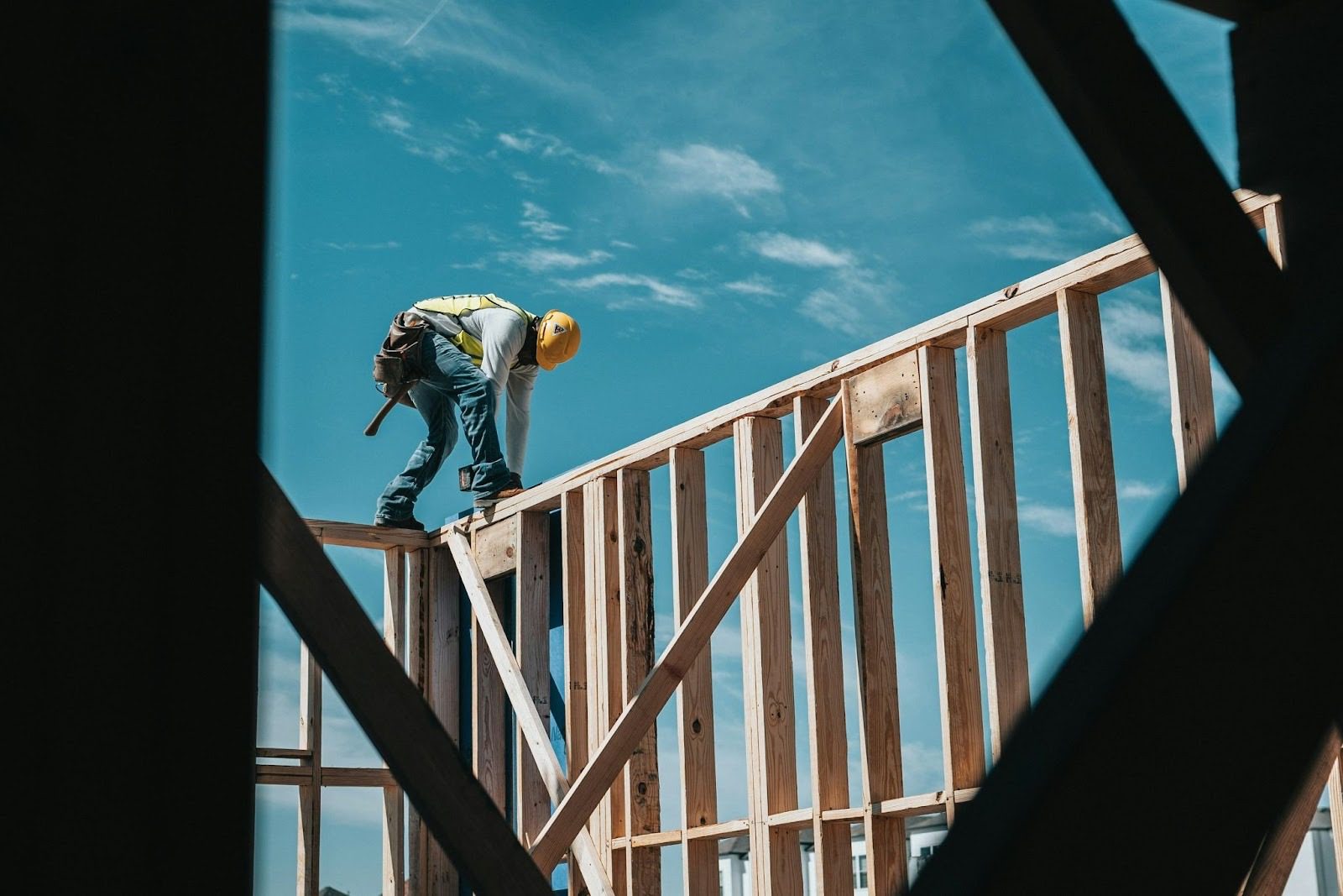 Construction worker standing on wooden framework under a blue sky. Is Building Your Own Home the Ultimate Dream or a Costly Mistake?