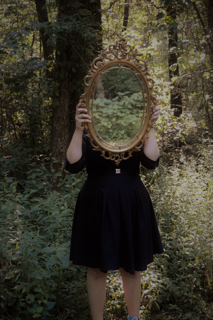 woman holding mirror against her head in the middle of forest 6 Empowering Ways to Reclaim How You Feel About Yourself