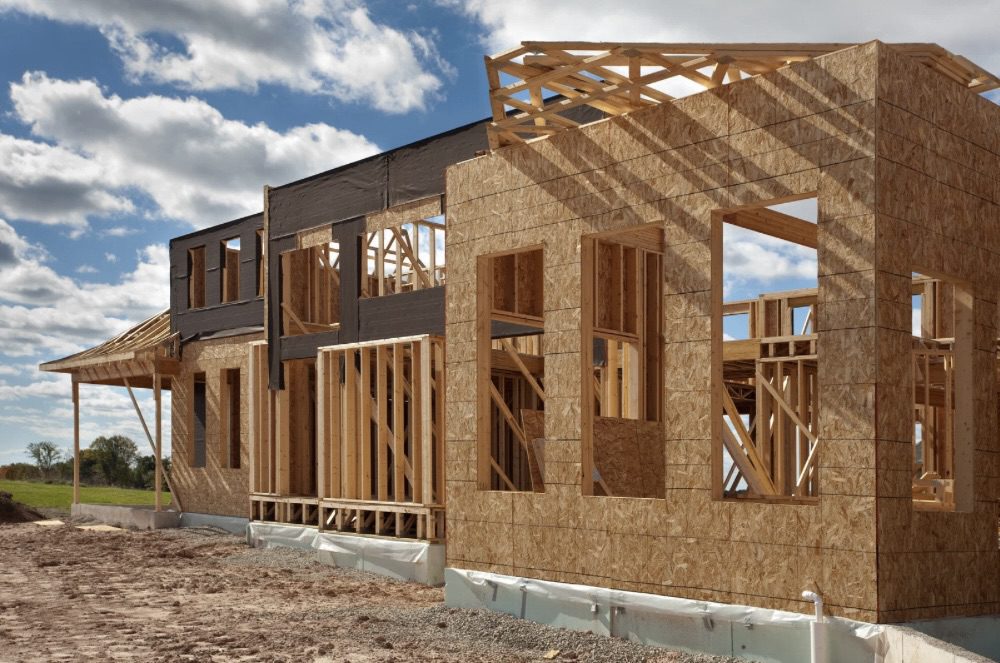 Construction site of a house showing wooden framing and walls in progress, with a clear blue sky and scattered clouds. Is Building Your Own Home the Ultimate Dream or a Costly Mistake?