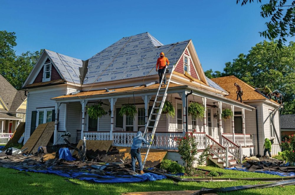A team of workers performing roofing repairs on a house, with scaffolding and materials around the property. Is Building Your Own Home the Ultimate Dream or a Costly Mistake?