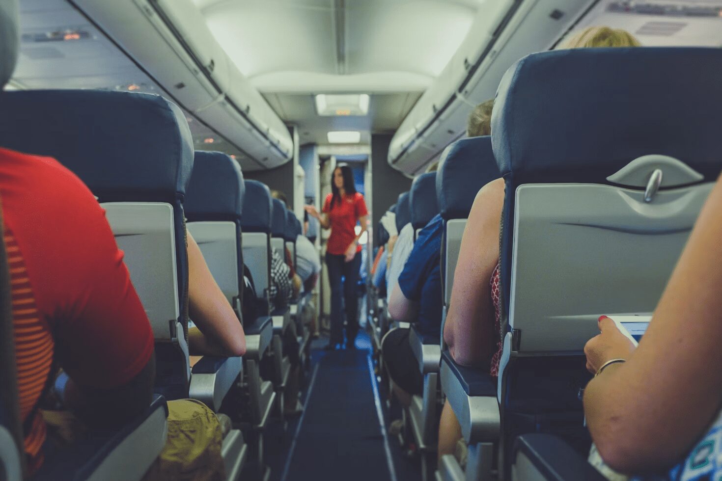 Interior view of an airplane with passengers seated and a flight attendant in red uniform walking down the aisle. 6 Careers That Let You Travel and Work At The Same Time