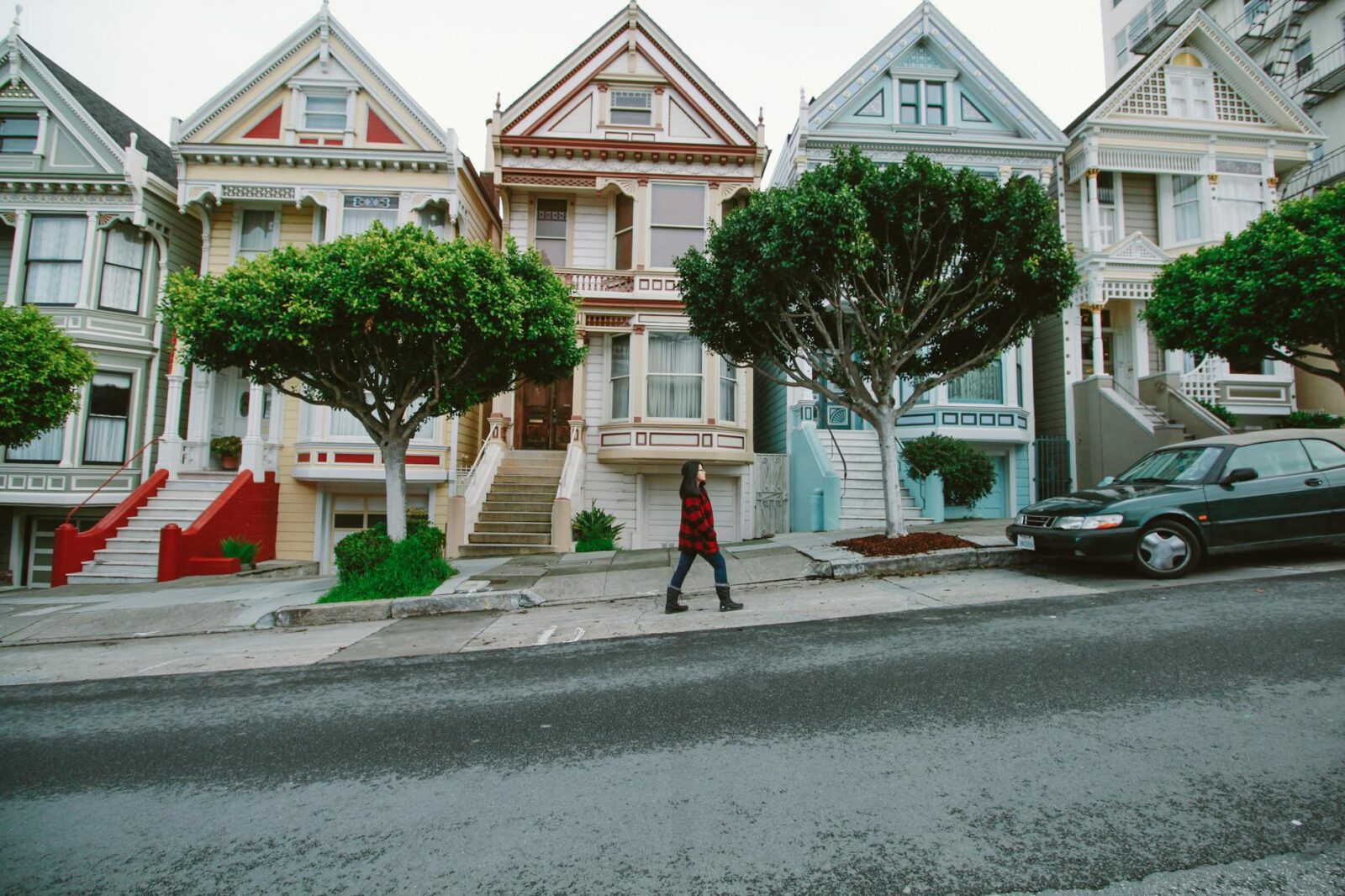 woman walking toward black sedan parked in front of colorful houses 7 Innovative Ways to Start Climbing the Property Ladder in 2025