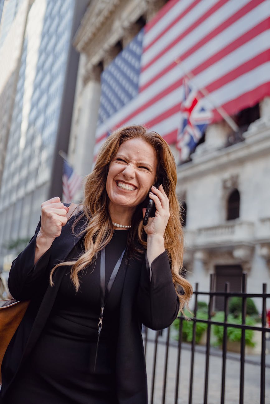 excited woman using mobile phone on a street and us flag in background Best Airlines to Fly Business Class to the UK from the USA (2026 Guide)